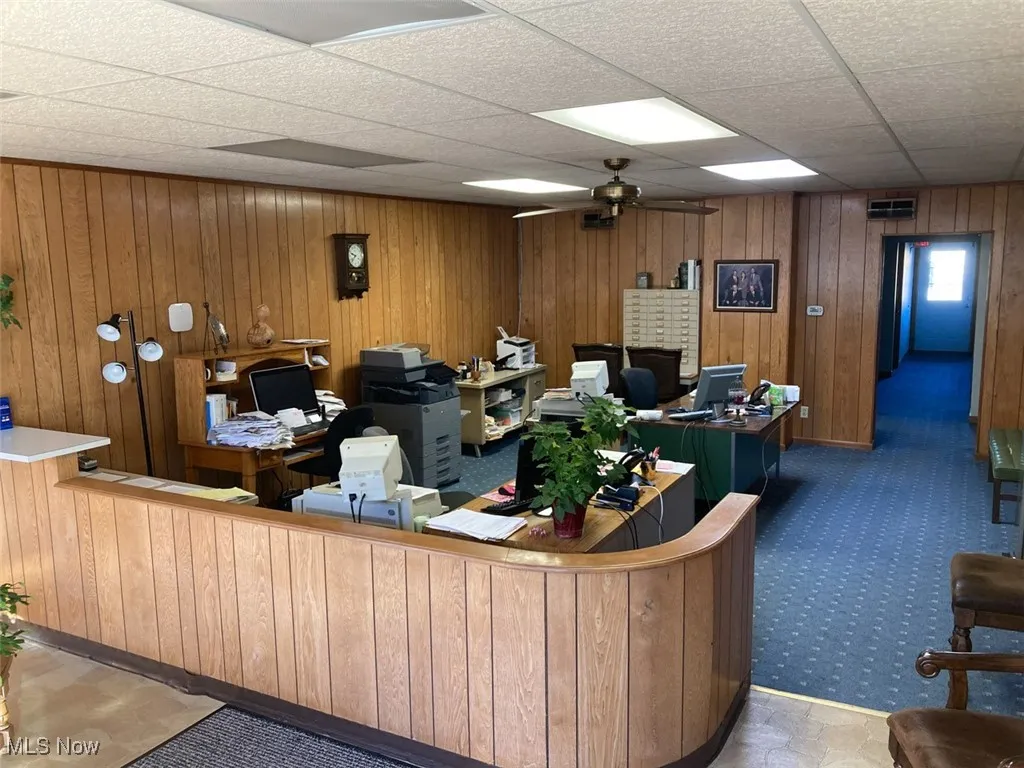 Reception featuring ceiling fan, wood walls, and a drop ceiling