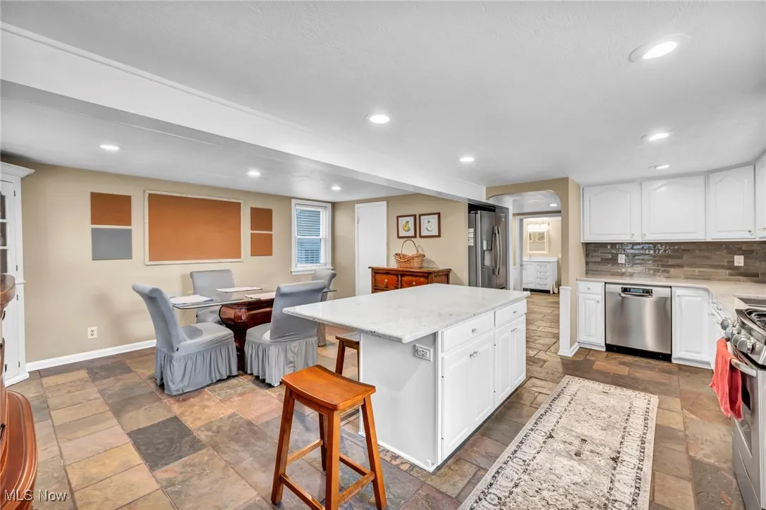 Kitchen featuring white cabinetry, a breakfast bar, light stone countertops, decorative backsplash, and recessed lighting