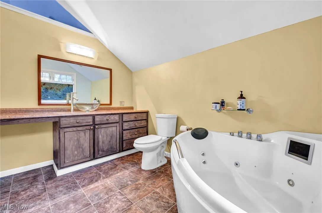 Full bath featuring a whirlpool tub, vaulted ceiling, and vanity