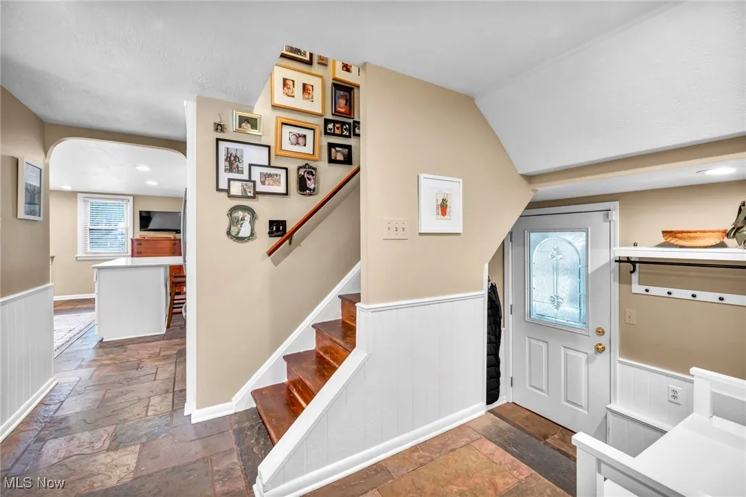 Foyer entrance featuring wainscoting, stone tile floors, arched walkways, and recessed lighting