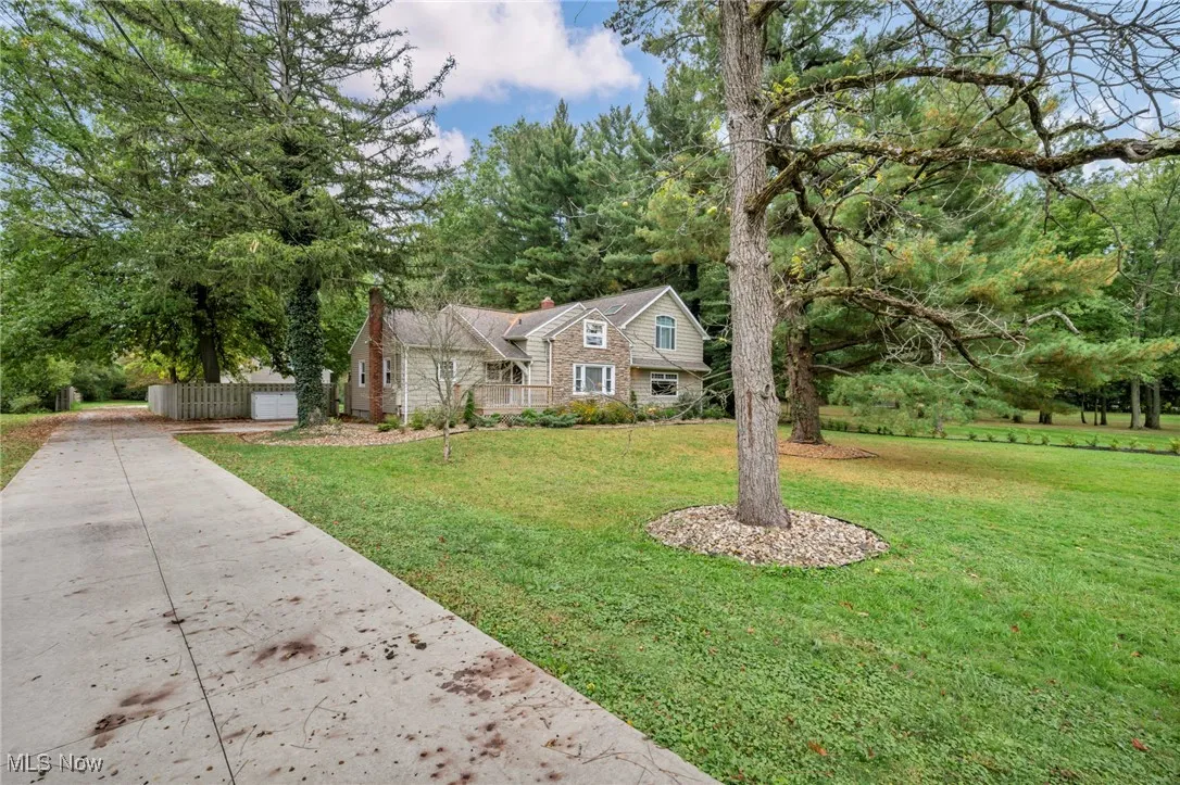 View of front facade with a chimney, a front lawn, concrete driveway, view of wooded area, and a garage