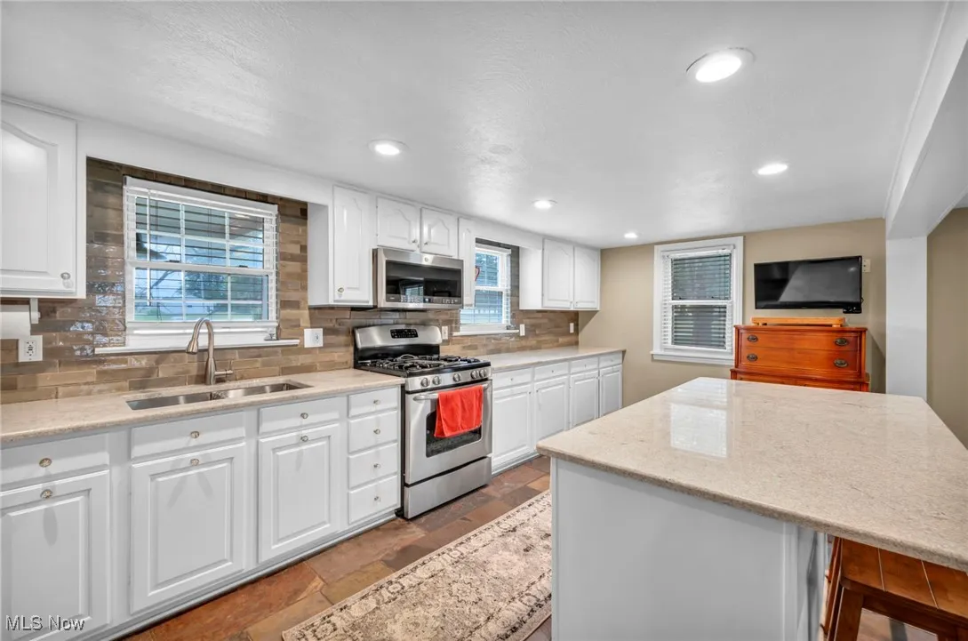 Kitchen with white cabinets, stainless steel appliances, light stone countertops, backsplash, and recessed lighting