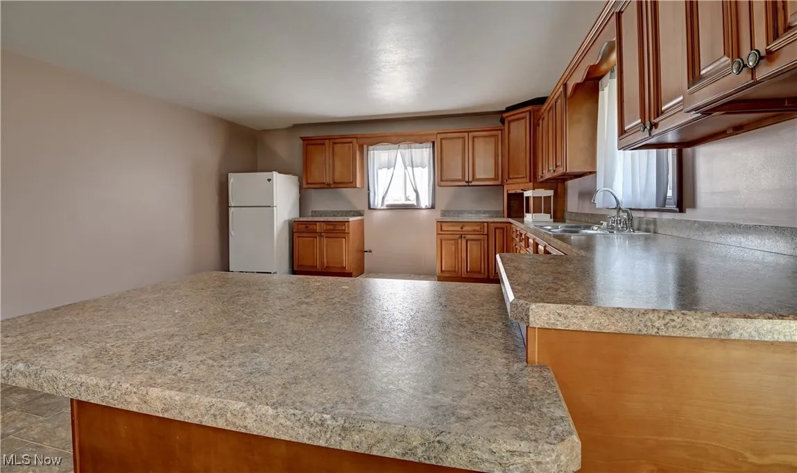 Kitchen with brown cabinetry, freestanding refrigerator, and light countertops