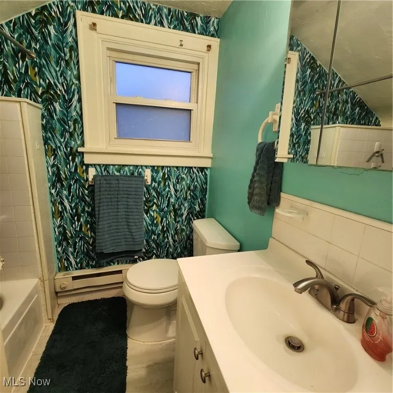 Bathroom featuring vanity, wallpapered walls, baseboard heating, and tasteful backsplash