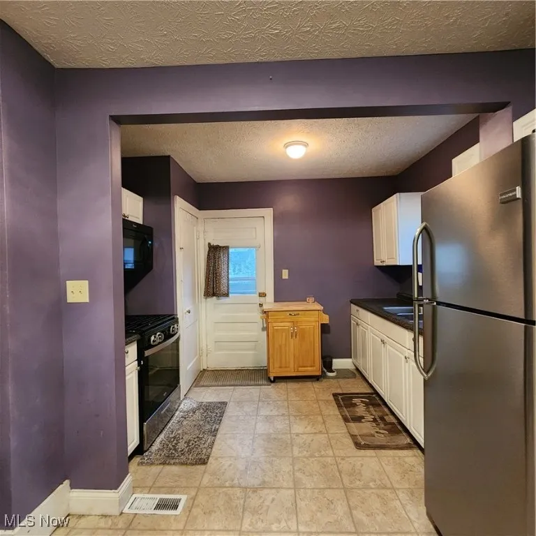 Kitchen with dark countertops, a textured ceiling, refrigerator, range, and white cabinetry