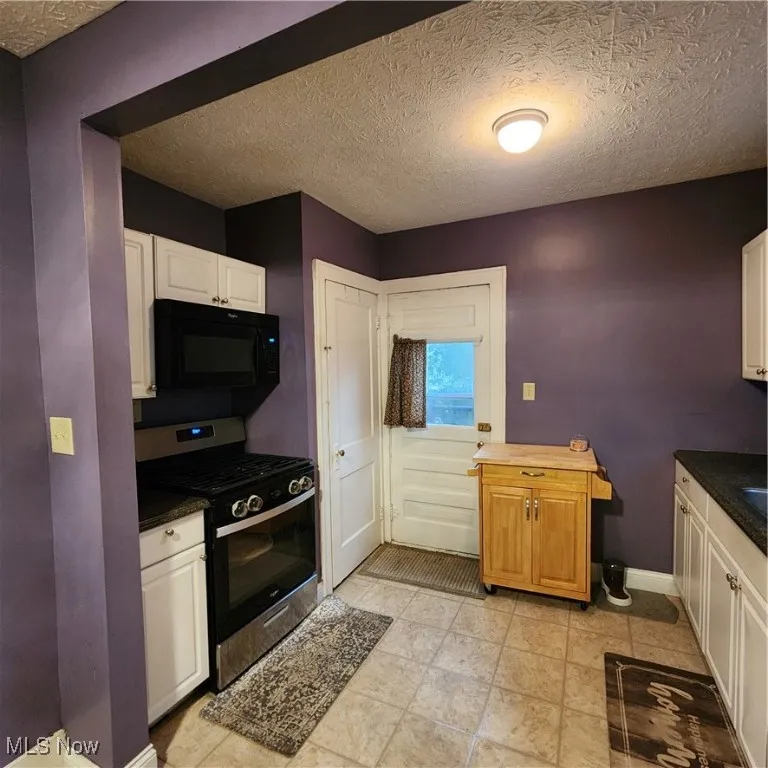 Kitchen featuring a textured ceiling, stove, and white cabinets