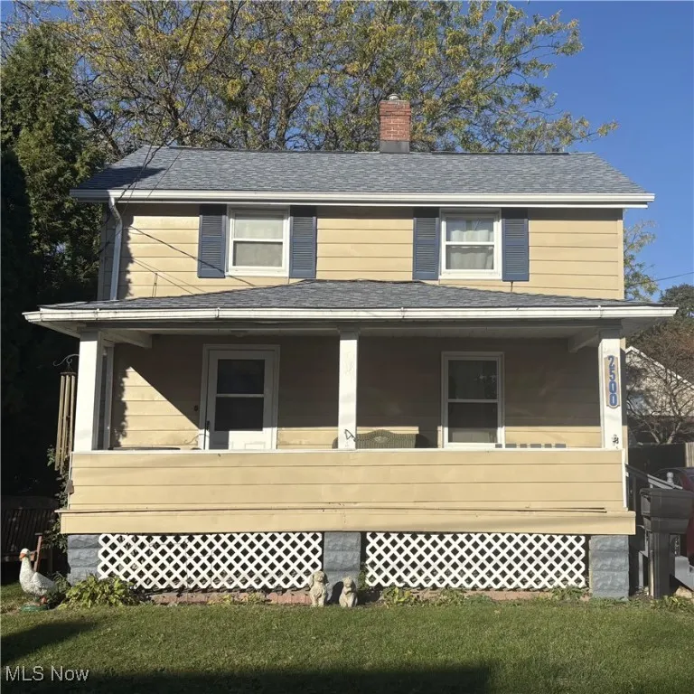 View of front of property featuring covered porch, a chimney, a front yard, and roof with shingles