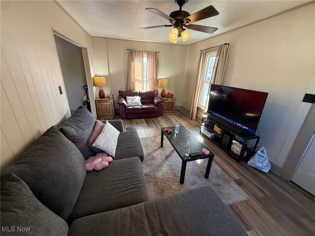 Living room with dark wood-type flooring, ceiling fan, and ornamental molding