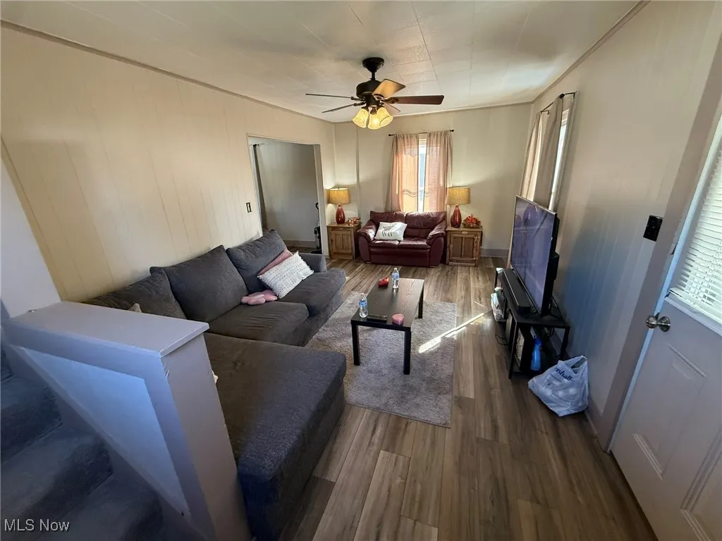Living room with dark wood-type flooring, ceiling fan, and wood walls