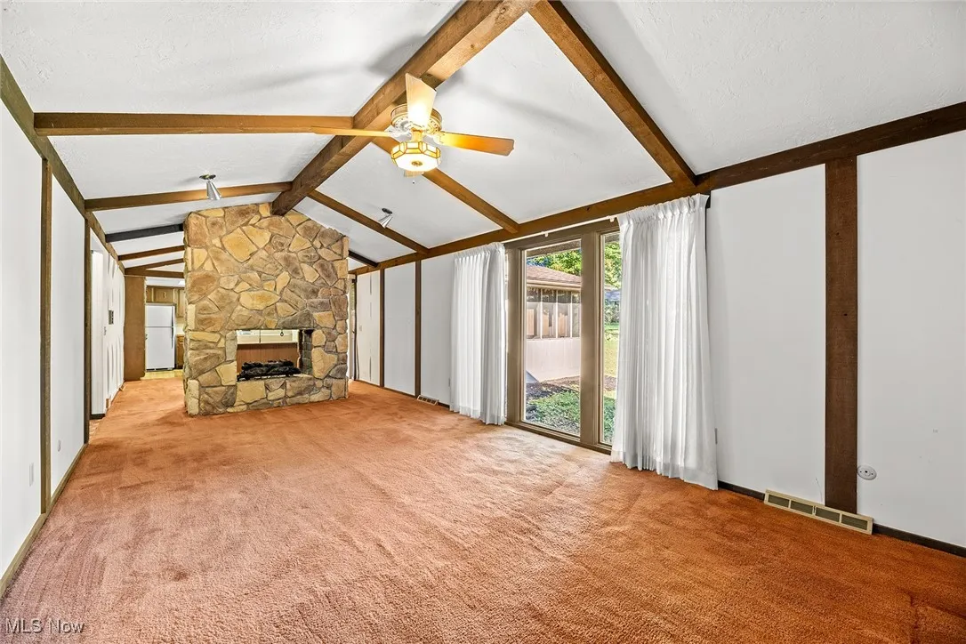 Unfurnished living room with a stone fireplace, carpet flooring, and ceiling fan