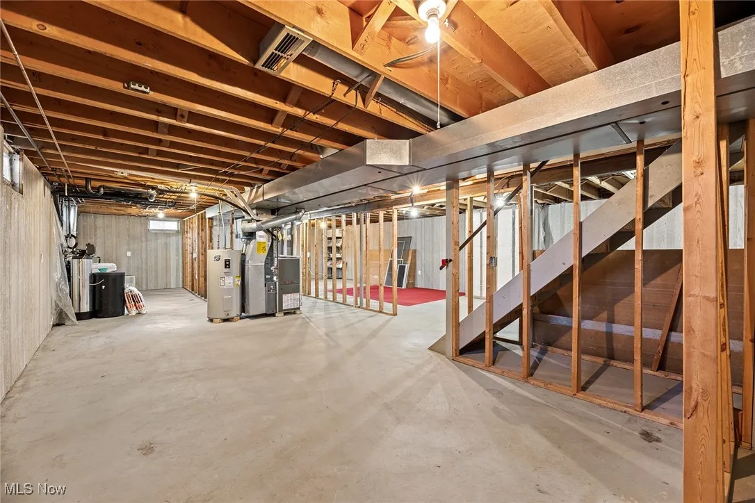 Unfinished basement featuring stairs, water heater, heating unit, and a water softener