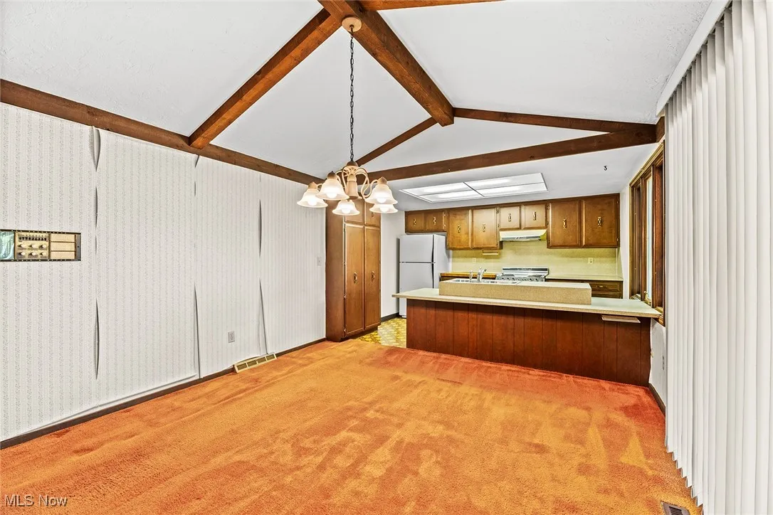 Kitchen featuring light countertops, a chandelier, light carpet, and brown cabinetry
