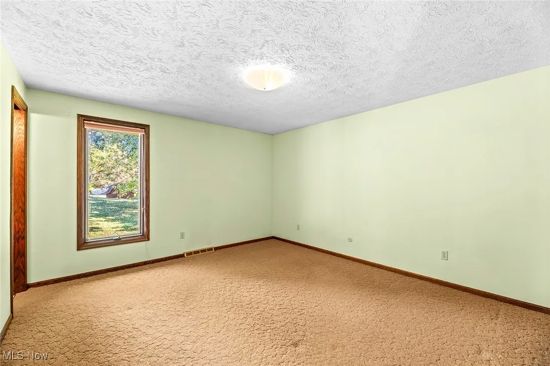 Carpeted spare room featuring a textured ceiling and baseboards