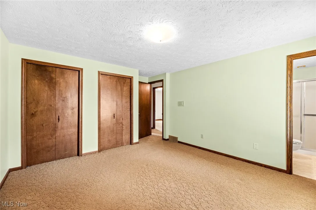 Unfurnished bedroom featuring multiple closets, light colored carpet, a textured ceiling, and ensuite bath