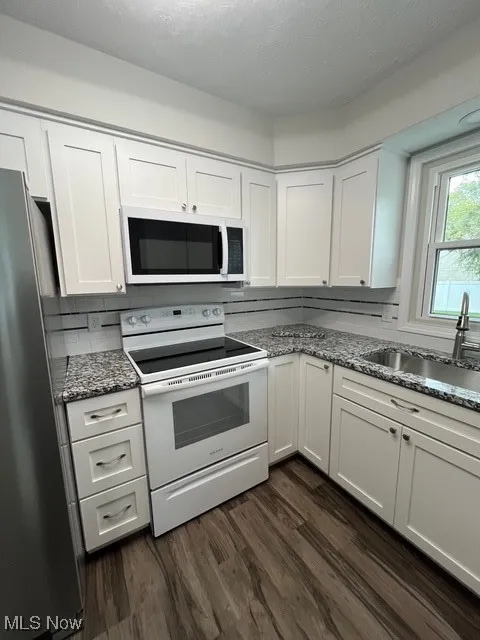 Kitchen featuring white stove, white cabinetry, light stone counters, fridge, and dark wood-type flooring