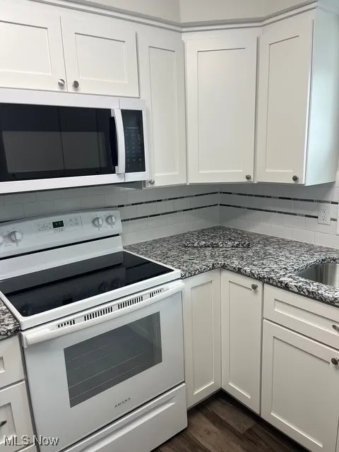 Kitchen with white range oven, white cabinetry, backsplash, and dark stone counters