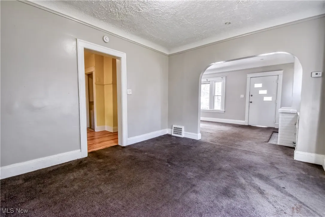 Empty room with dark carpet, a textured ceiling, and arched walkways