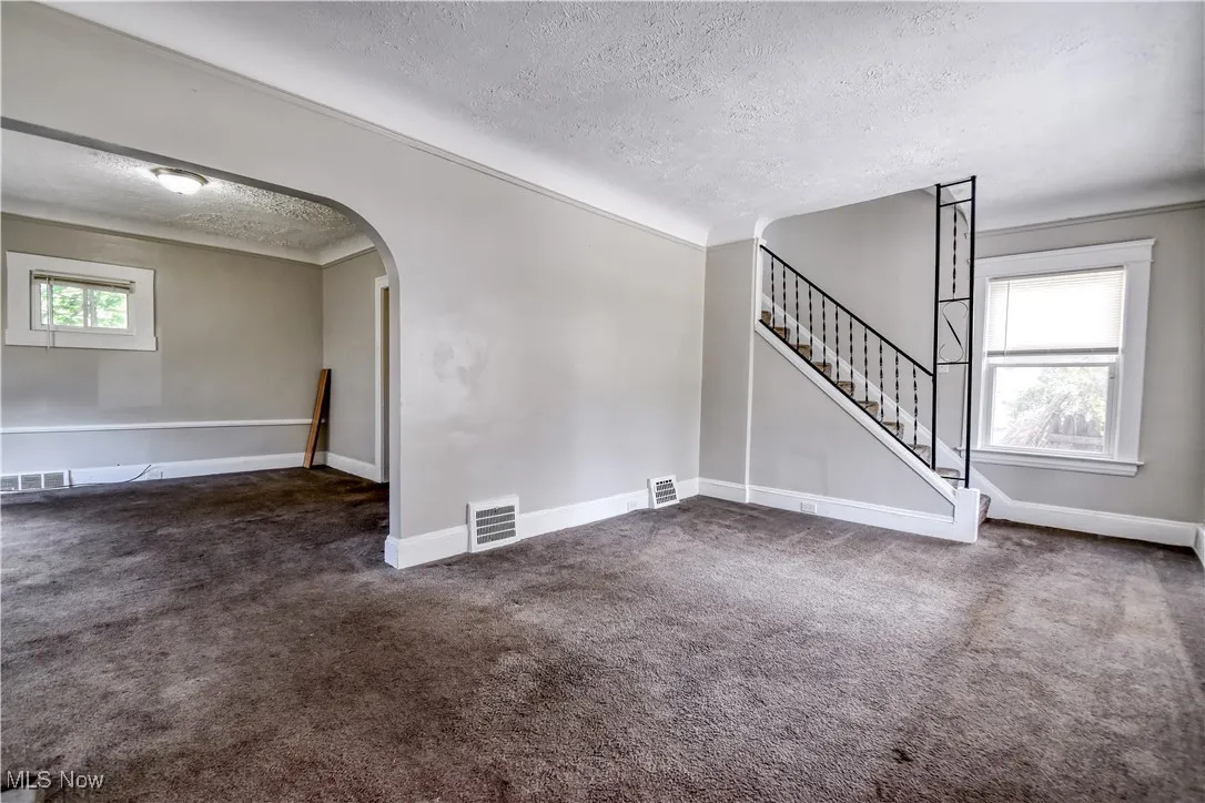 Carpeted empty room with a textured ceiling, arched walkways, stairway, and crown molding