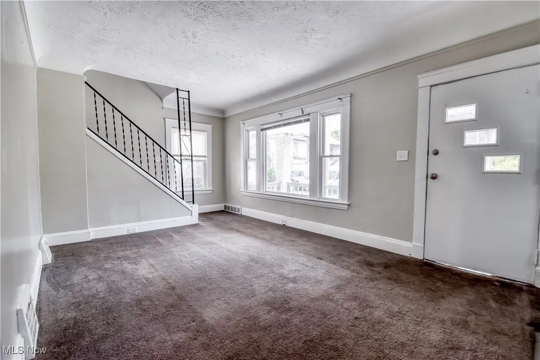 Unfurnished living room with stairs, a textured ceiling, carpet floors, and crown molding