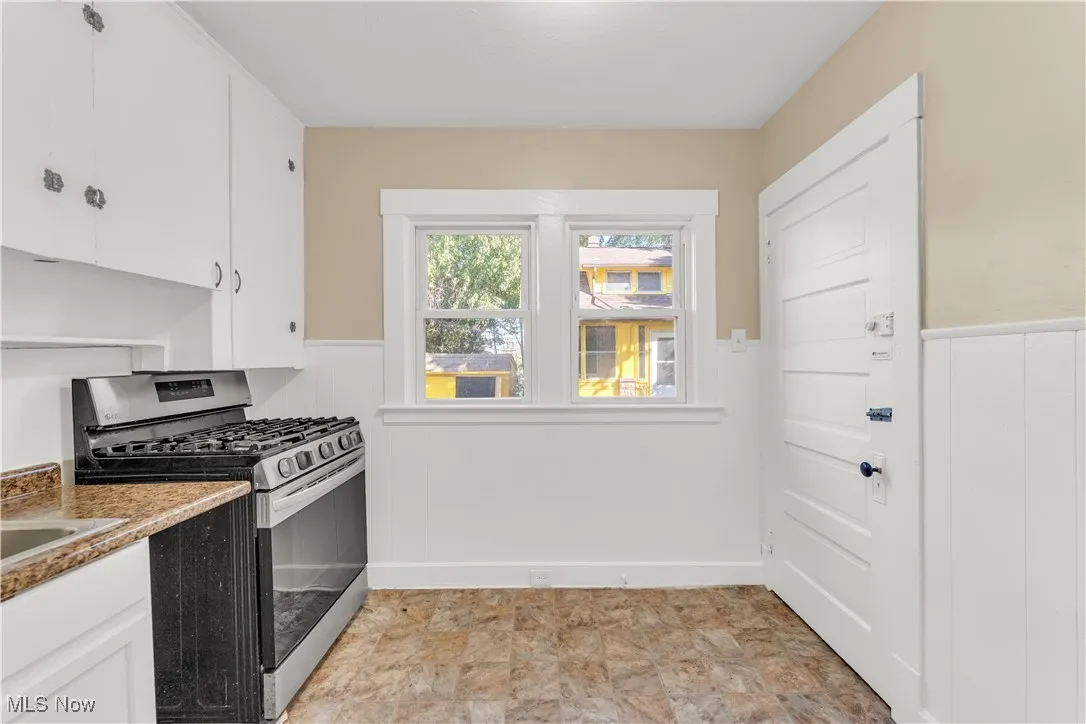 Kitchen featuring stainless steel gas range, white cabinets, wainscoting, wooden walls, and stone finish flooring