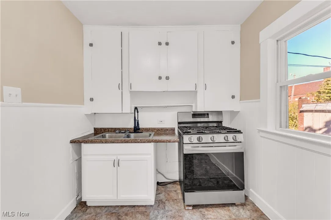 Kitchen with gas range, white cabinets, dark countertops, and wainscoting