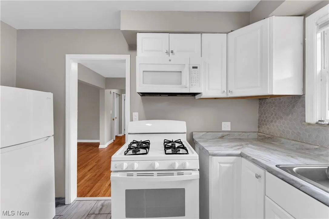 Kitchen featuring white appliances, light countertops, white cabinetry, decorative backsplash, and light wood-style​​‌​​​​‌​​‌‌​‌‌​​​‌‌​‌​‌​‌​​​‌​​ flooring