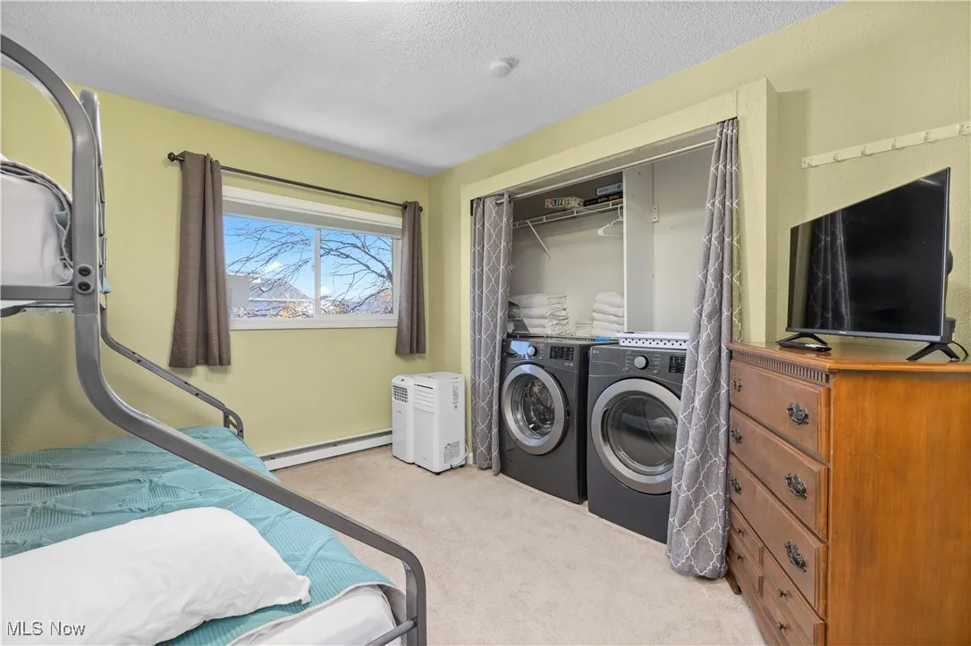 Bedroom featuring light carpet, a textured ceiling, independent washer and dryer, a baseboard radiator, and a closet