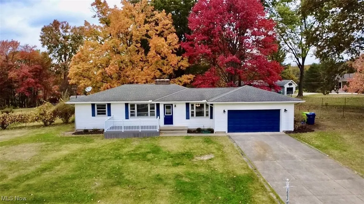 Ranch-style house featuring a garage, driveway, a front yard, a chimney, and view of wooded area