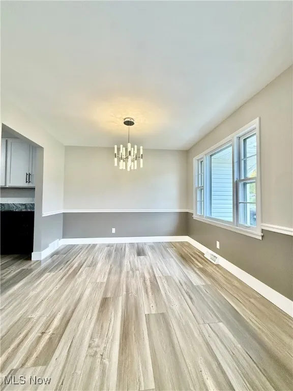 Unfurnished dining area featuring light wood-style flooring and a chandelier