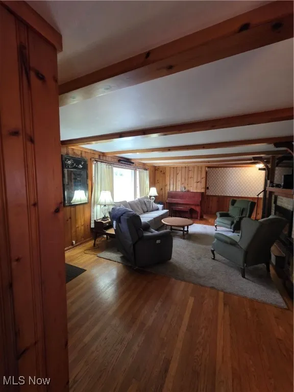 Living room with beam ceiling, dark wood-type flooring, and wooden walls