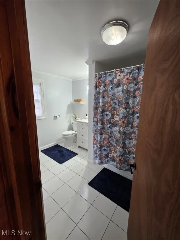 Bathroom featuring light tile patterned floors, curtained shower, ornamental molding, and vanity