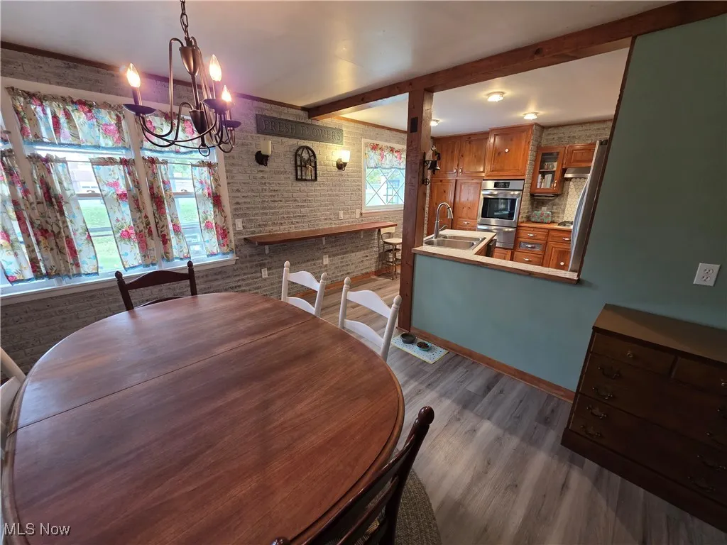 Dining room with brick wall, dark wood-type flooring, a chandelier, and beam ceiling