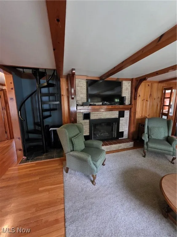 Living room featuring beamed ceiling, a fireplace, wood finished floors, wood walls, and stairs