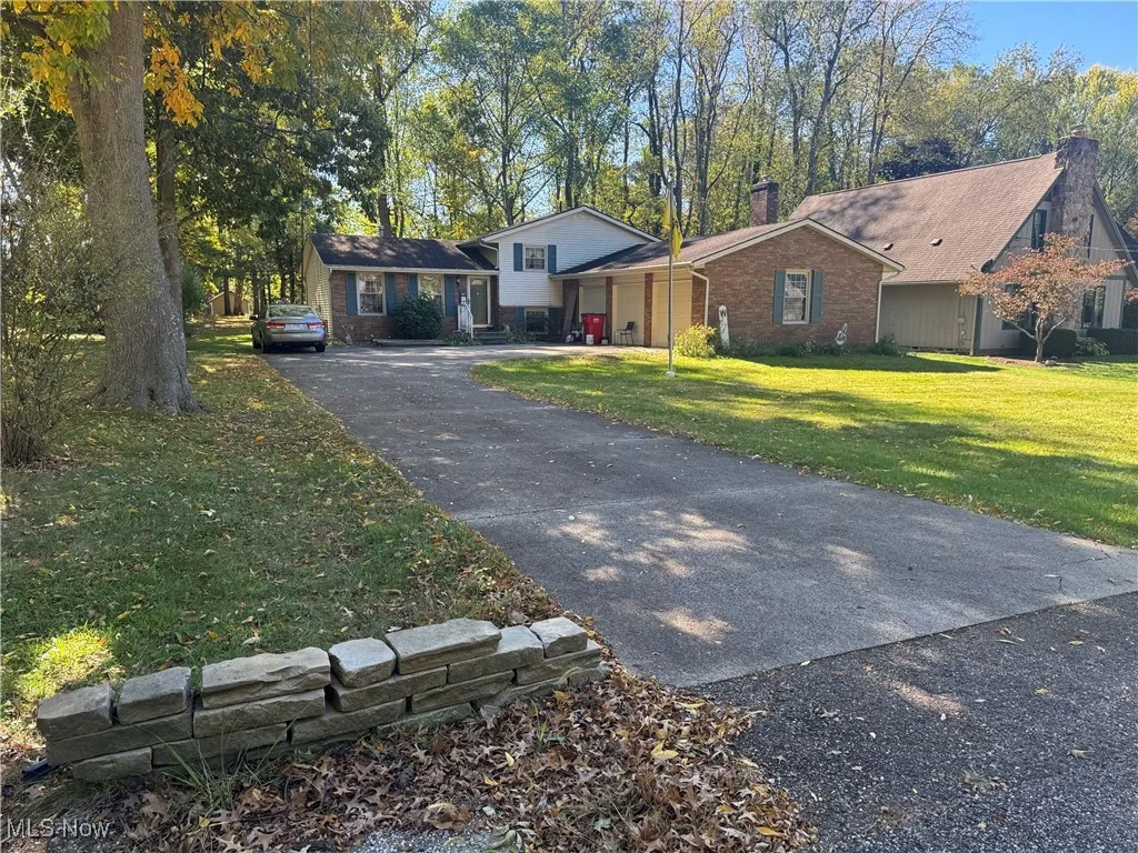 Tri-level home featuring a chimney, asphalt driveway, a front yard, brick siding, and a garage