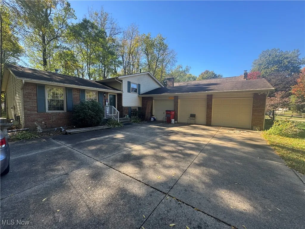 Tri-level home featuring brick siding, driveway, an attached garage, and a chimney
