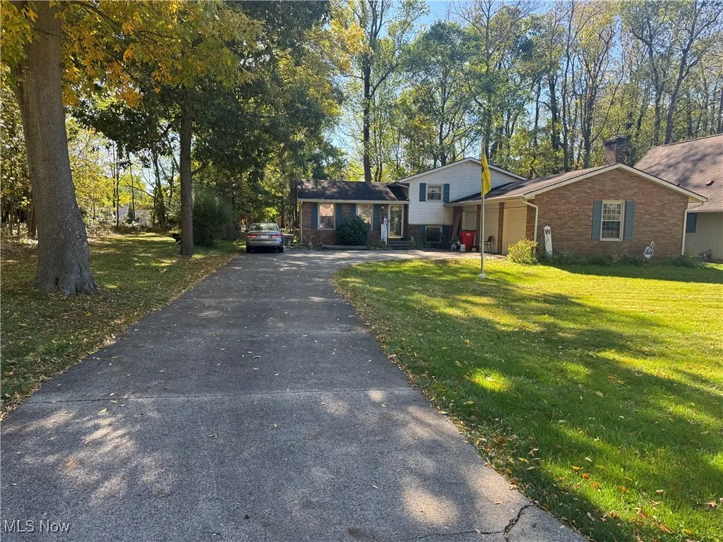 Tri-level home featuring a chimney, a front yard, driveway, and brick siding