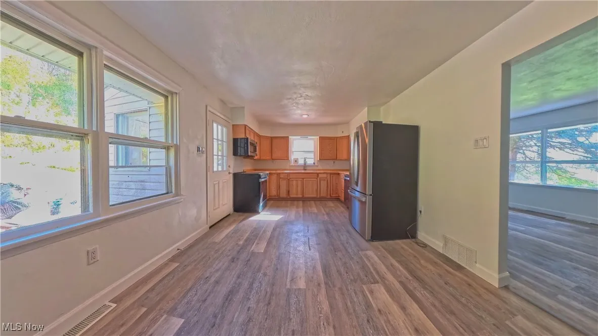 Kitchen with freestanding refrigerator, dark wood-type flooring, brown cabinets, and light countertops