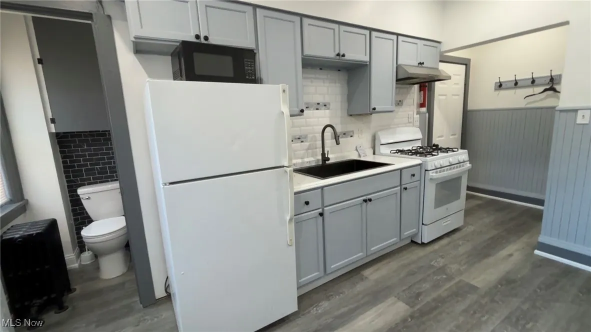 Kitchen with white appliances, wainscoting, gray cabinetry, wood finished floors, and light countertops