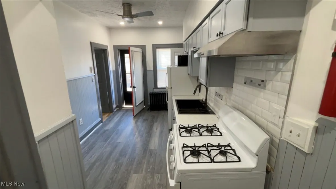 Kitchen featuring white gas range, a wainscoted wall, under cabinet range hood, dark wood-style flooring, and a textured ceiling