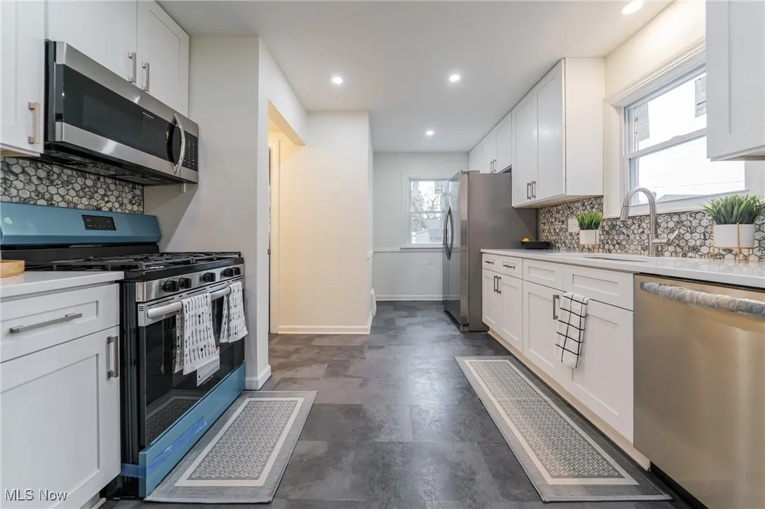 Kitchen with decorative backsplash, appliances with stainless steel finishes, white cabinets, and recessed lighting
