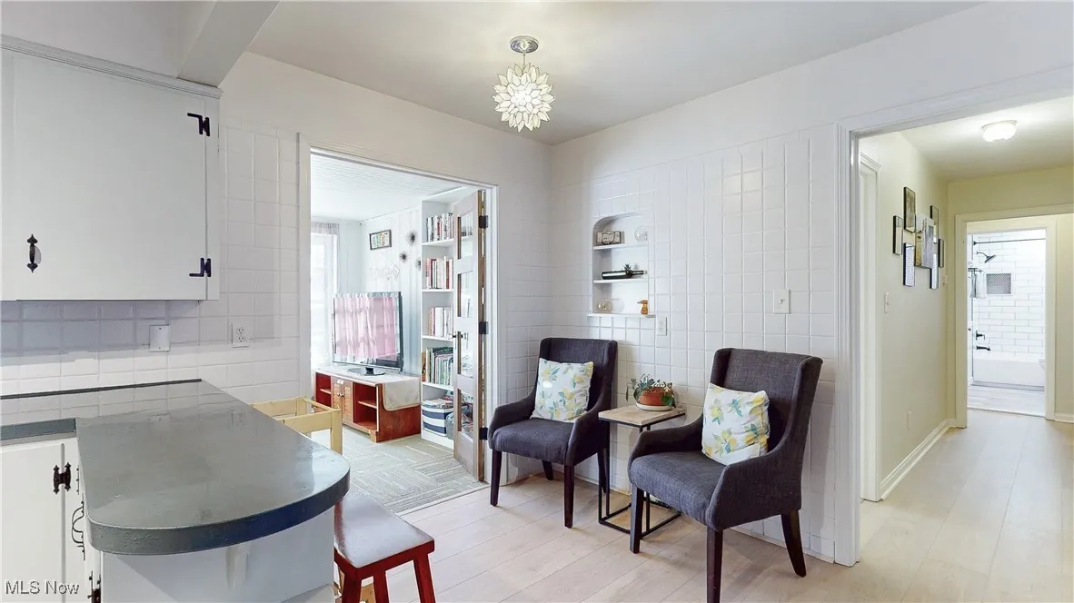 Living area with tile walls, light wood-style flooring, and a chandelier