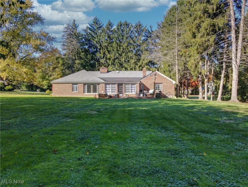 Back of property featuring a chimney, a yard, brick siding, and view of wooded area