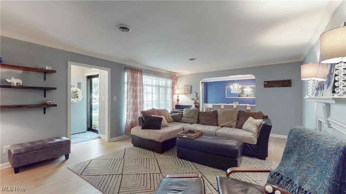 Living area featuring wood finished floors, crown molding, arched walkways, and a chandelier