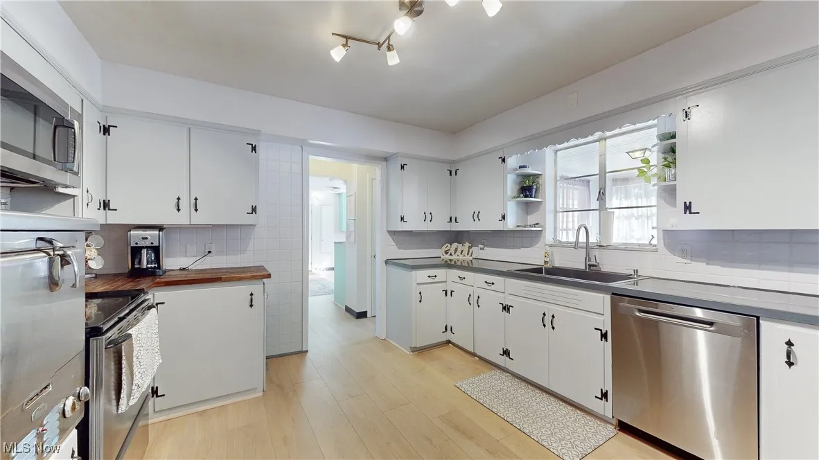 Kitchen featuring backsplash, open shelves, stainless steel appliances, white cabinetry, and dark countertops