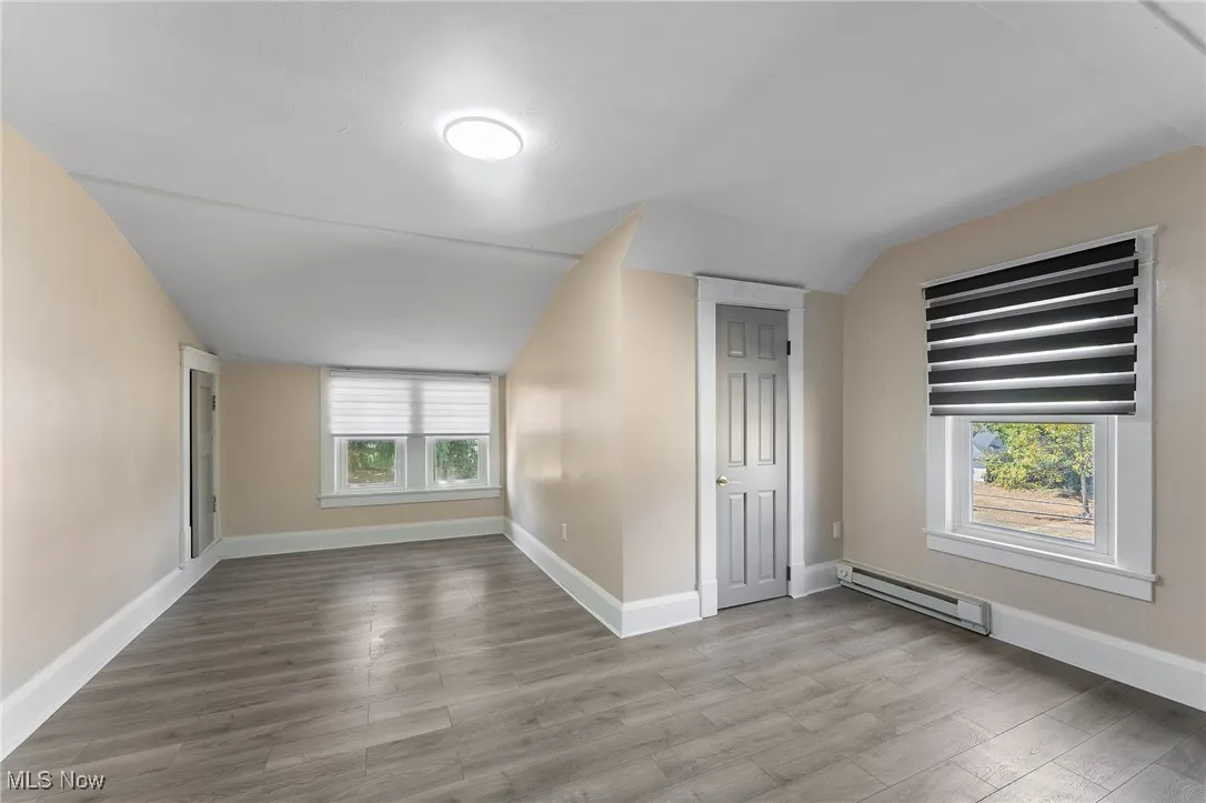 Additional living space featuring a baseboard radiator, vaulted ceiling, and light wood-type flooring