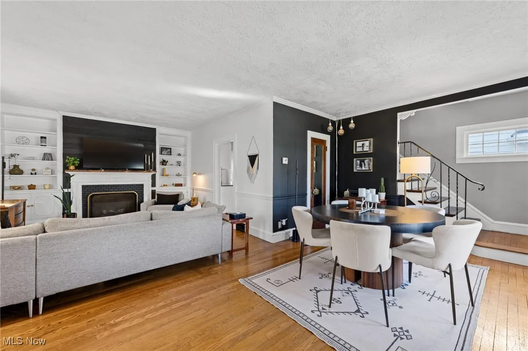Dining room with light wood-style floors, a textured ceiling, stairway, a brick fireplace, and ornamental molding