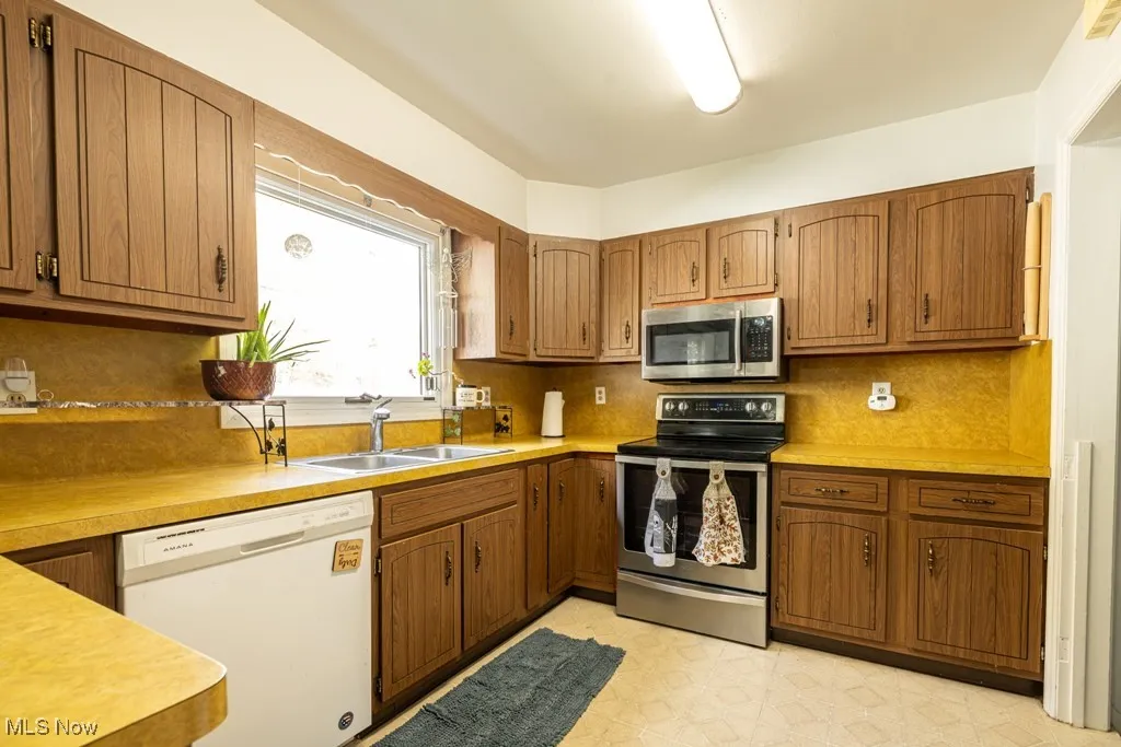 Kitchen with stainless steel appliances, backsplash, light countertops, and brown cabinetry