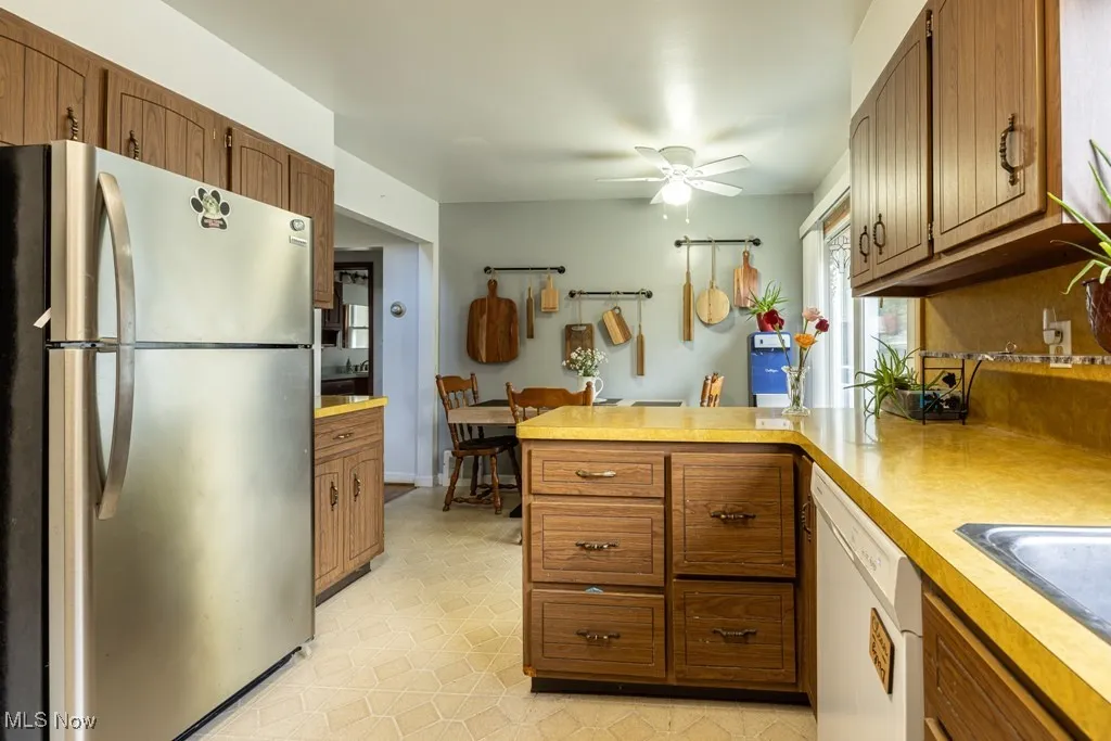 Kitchen featuring freestanding refrigerator, light countertops, dishwasher, a peninsula, and a ceiling fan