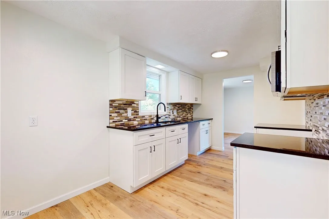 Kitchen featuring tasteful backsplash, white cabinets, light wood-style floors, stainless steel microwave, and dark stone counters