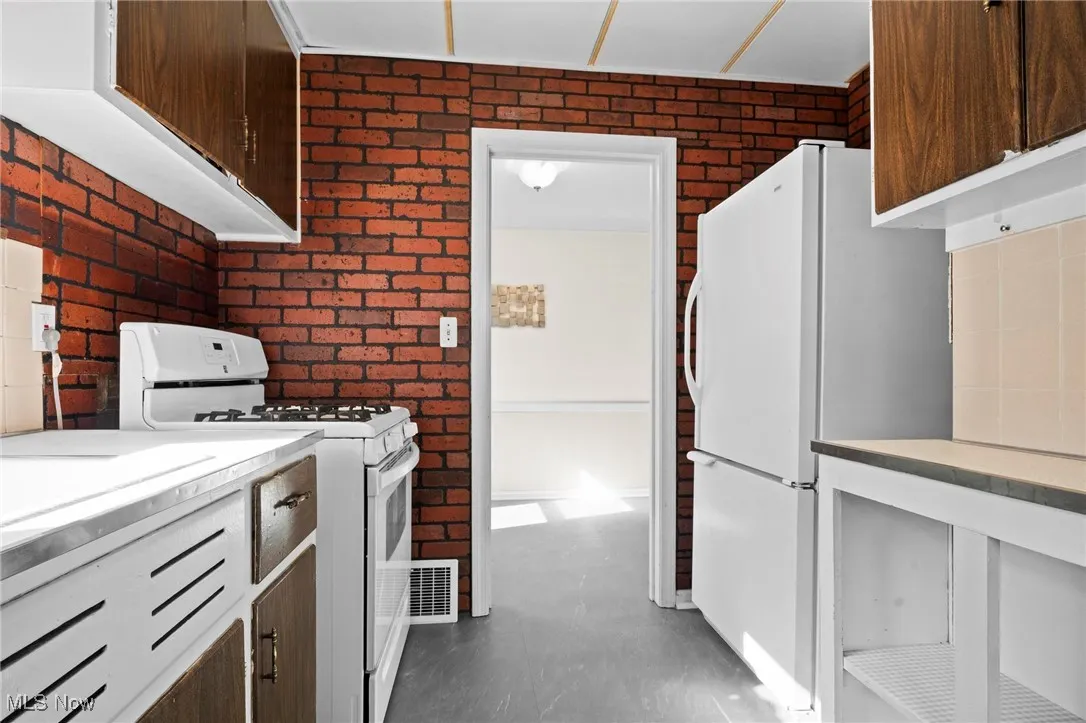 Kitchen with white appliances, brick wall, light countertops, and dark brown cabinetry